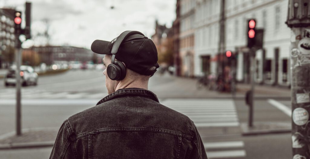 A young man in a cap and headphones waits at a city crosswalk, embracing modern lifestyle.